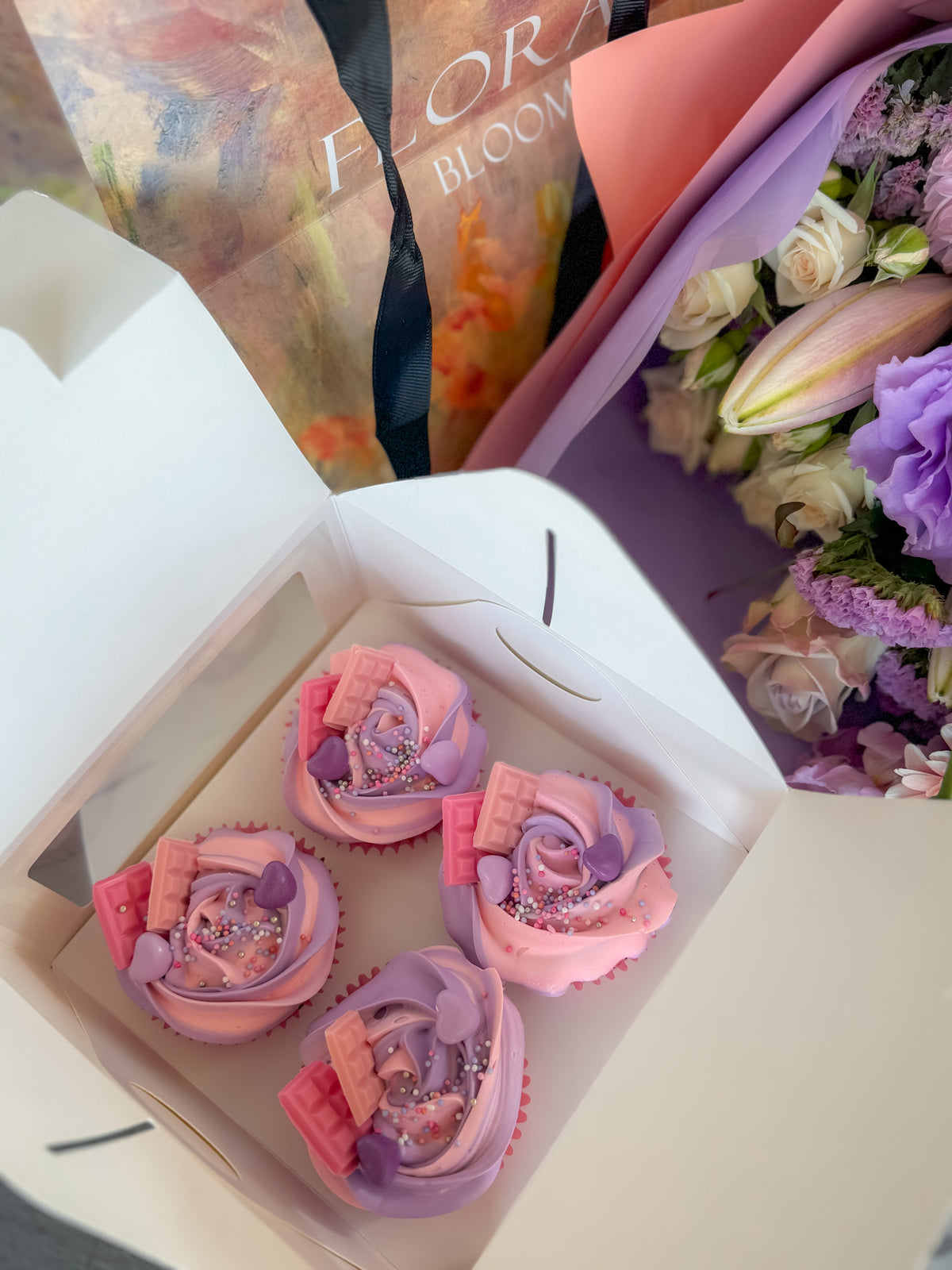 Decorative cupcakes in a box with flowers in the background