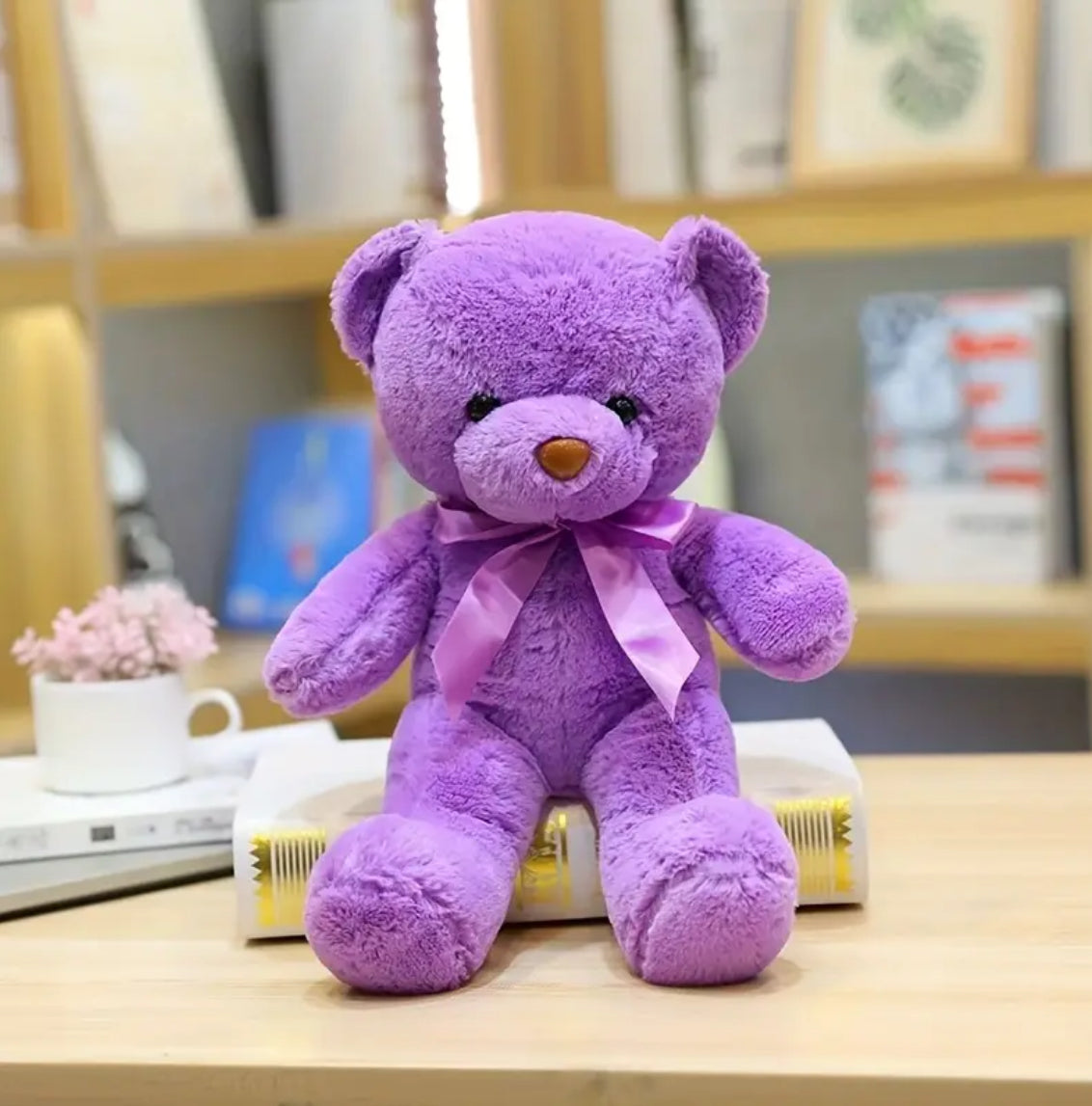A purple-coloured teddy bear with a satin ribbon bow around its neck.