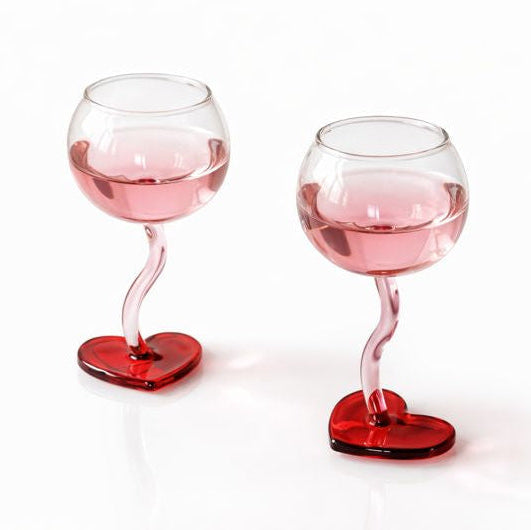 Two wine glasses with pink liquid and red bases on a white background