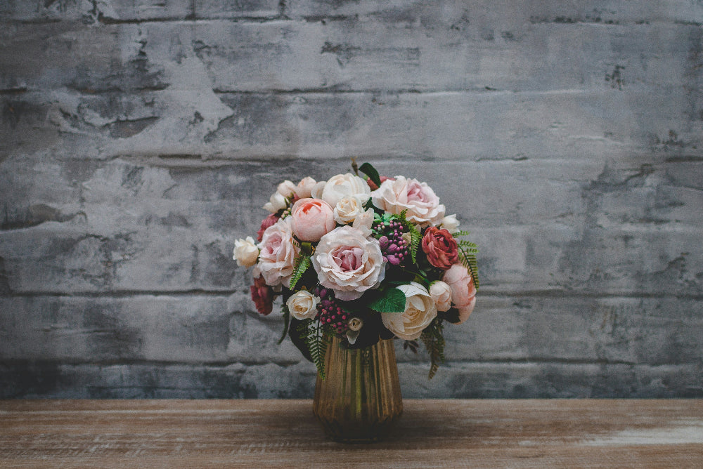 Bouquet of flowers in a vase against a textured stone wall.