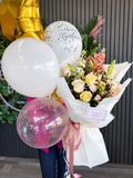 Pastel birthday bouquet with cream roses, peach orchids, white wrapping, pink ribbon and birthday balloons