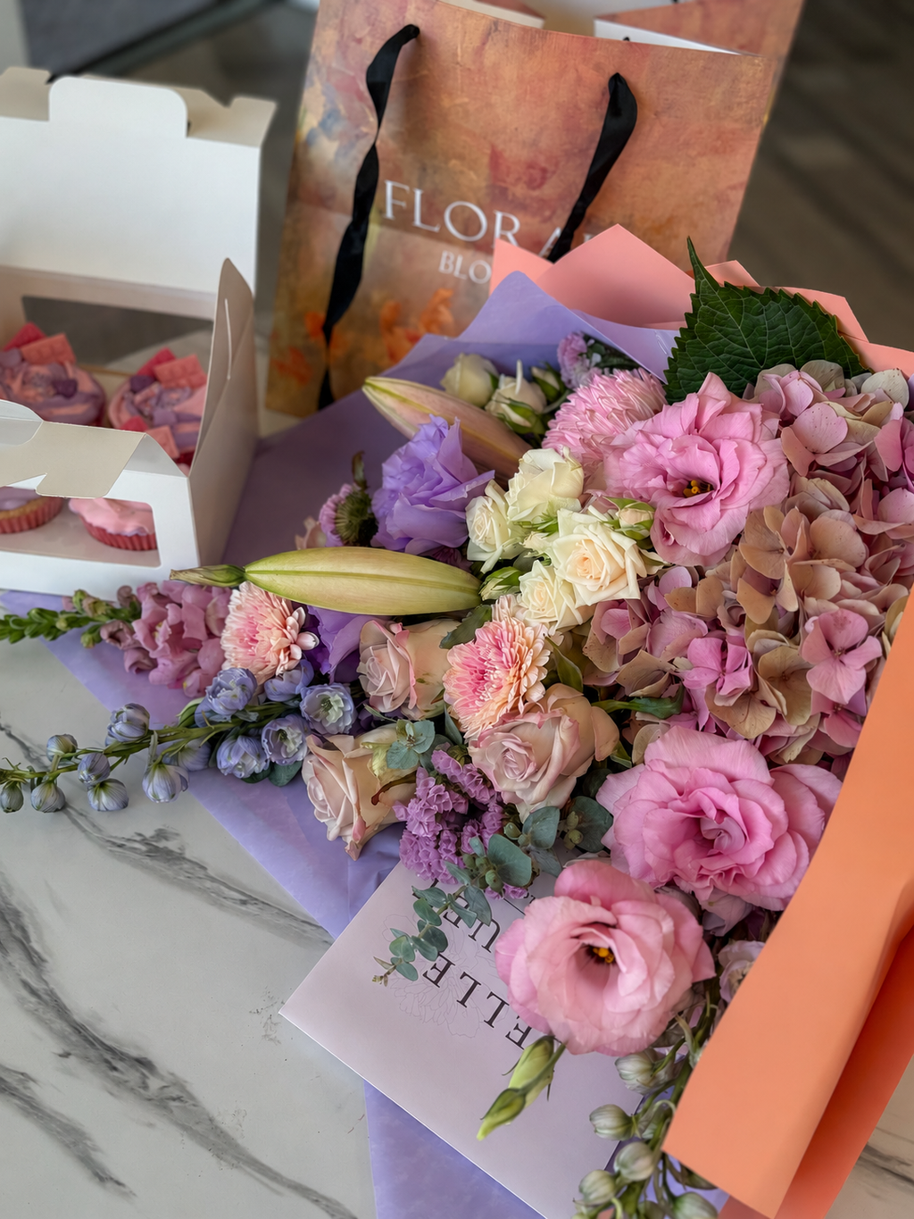 Natural close-up of pink hydrangea, lisianthus, cream roses and closed lily buds in lilac and peach wrapping