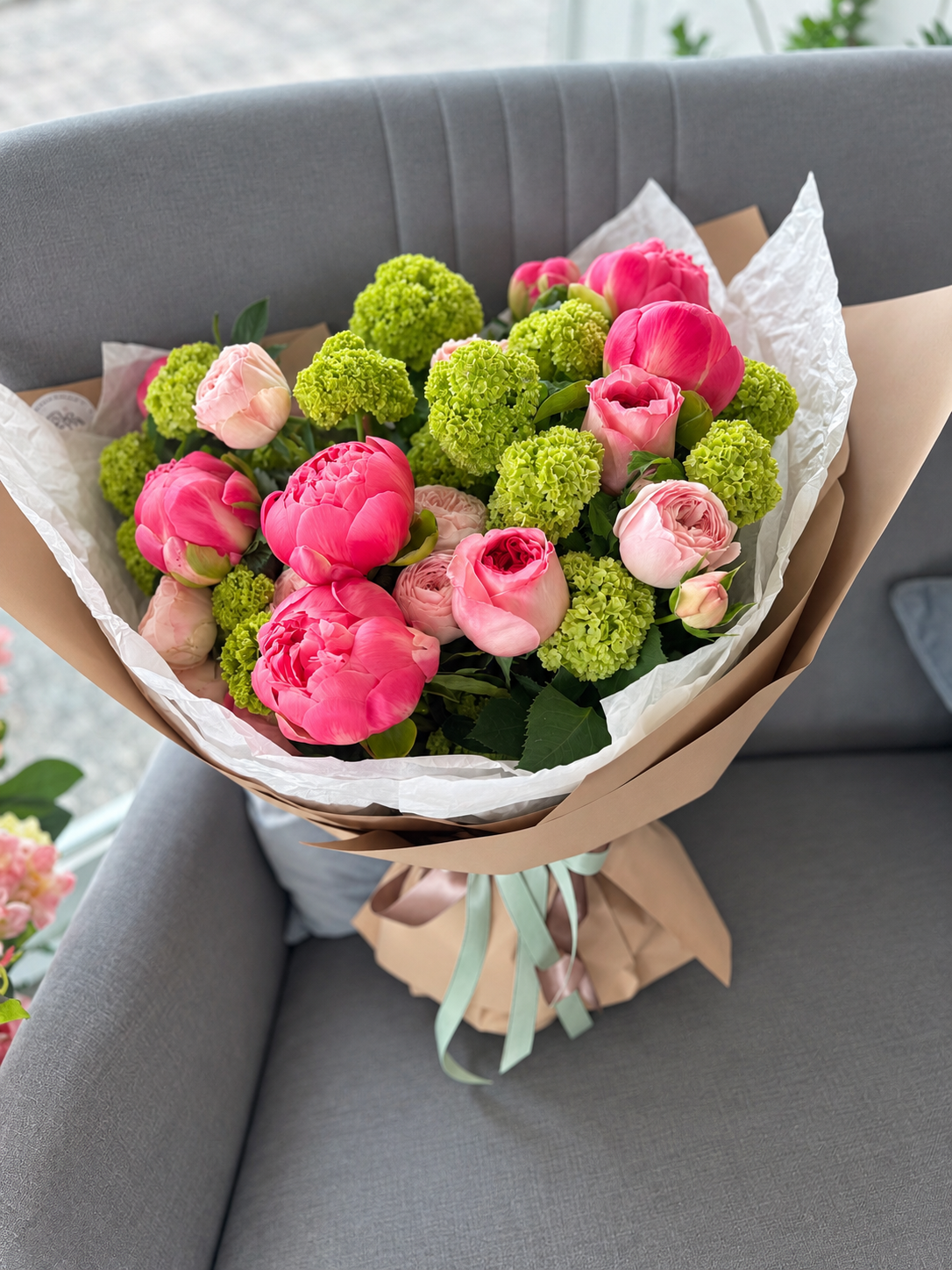 Pink peonies, blush garden roses and lime-green viburnum in taupe wrapping with mint ribbons
