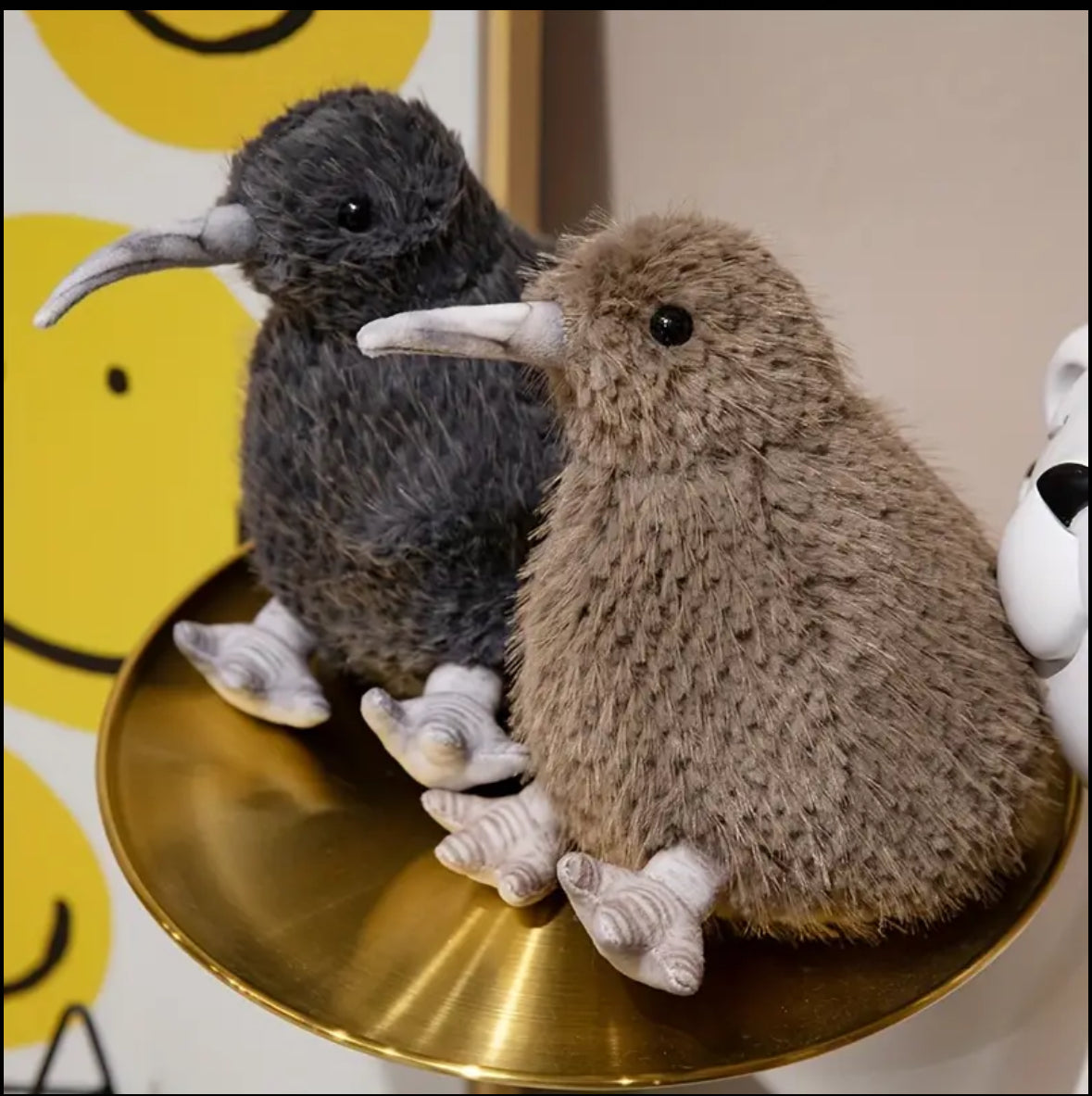 Two plush kiwi birds on a gold stand with a colorful background